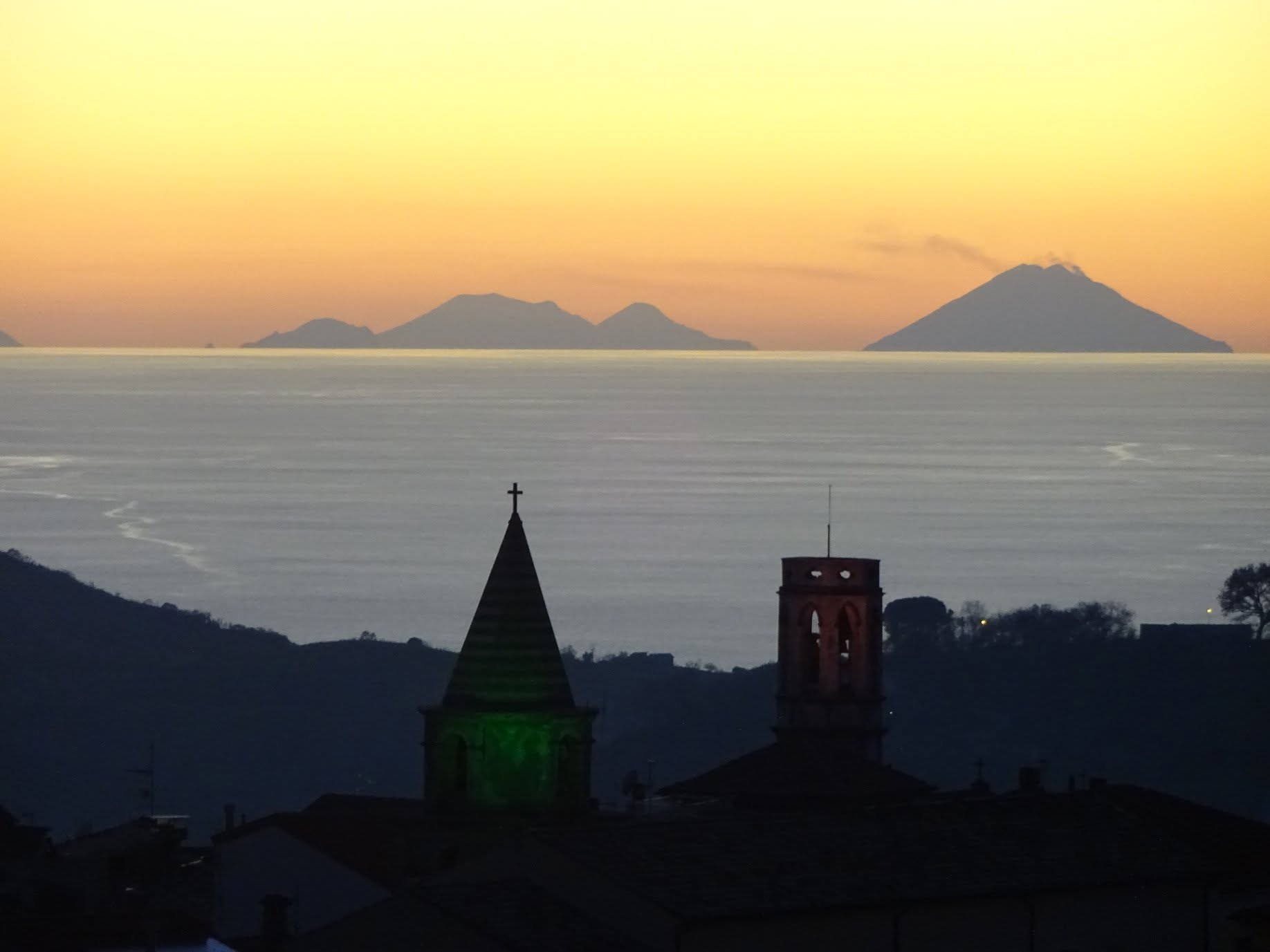 Sunset over Lago, Calabria: the village bell towers silhouetted against the Tyrrhenian Sea, with the Aeolian Islands and Stromboli on the horizon
